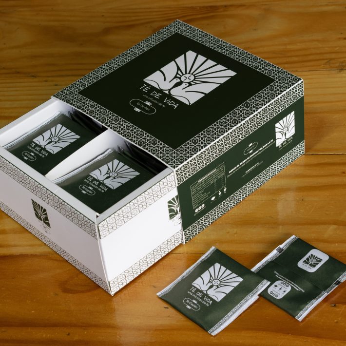 Caja abierta de Té de Vida Ceylán con 50 sachets individuales verdes, cada uno con un mensaje bíblico, sobre mesa de madera